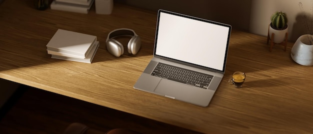 Espacio de trabajo con maqueta de computadora portátil, auriculares, taza de café, libros y decoración en una mesa de madera