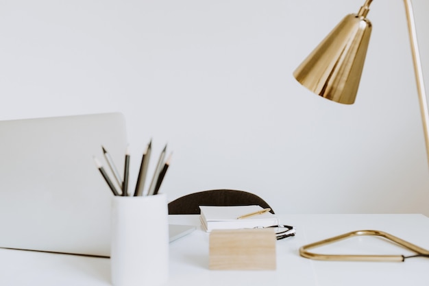 Espacio de trabajo de mesa de escritorio de oficina en casa escandinavo brillante con computadora portátil, lámpara, libros