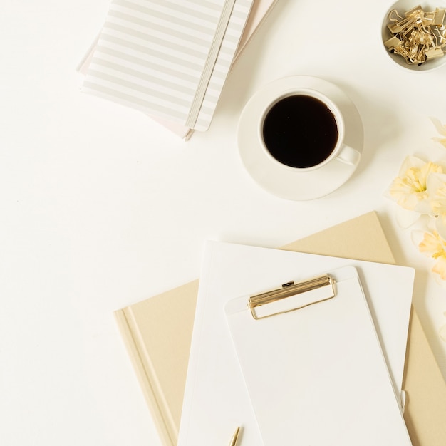 Espacio de trabajo de mesa de oficina en casa. Almohadilla de portapapeles de hoja en blanco con espacio de copia, taza de café, flores de narciso, papelería en blanco