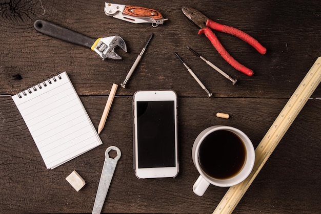 espacio de trabajo de la mesa de trabajo del técnico de vista superior con café negro y teléfono inteligente o tableta digital en blanco