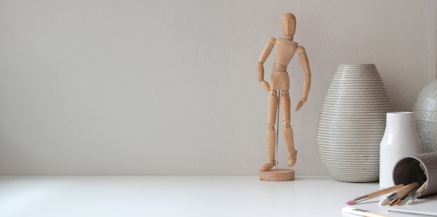 Espacio de trabajo mínimo con espacio de copia, figura de madera y florero de cerámica.