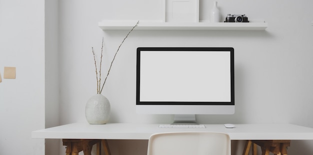 Espacio de trabajo moderno con computadora de escritorio de pantalla en blanco y decoraciones en mesa blanca y pared blanca