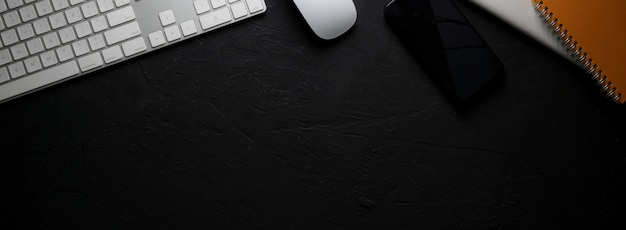Espacio de trabajo moderno oscuro con dispositivo de computadora, teléfono inteligente, cuadernos en mesa negra