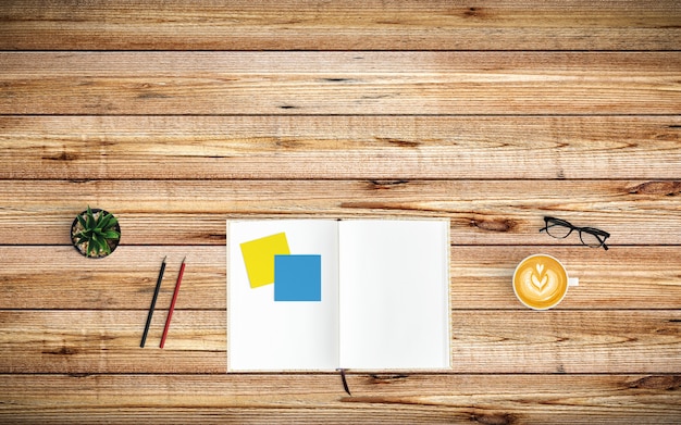 Espacio de trabajo moderno con taza de café, papel, cuaderno y lápices sobre madera.