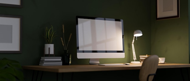 Espacio de trabajo de la oficina en casa por la noche con luz de maqueta de computadora de pc de la lámpara de mesa sobre la pared verde