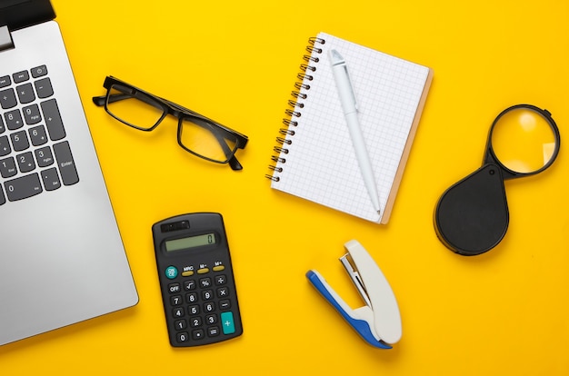 Espacio de trabajo de oficina con computadora portátil, calculadora, gafas, grapadora y cuaderno.