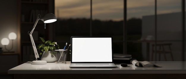 Un espacio de trabajo oscuro con luz de maqueta de computadora portátil de lámpara de mesa y accesorios en una mesa