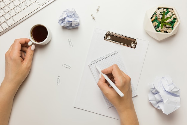 Espacio de trabajo con portapapeles en blanco, teclado, bolígrafo, bola de papel arrugada, cactus en una olla y taza de café