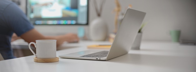 Espacio de trabajo portátil con computadora portátil abierta, taza de café y suministros en el escritorio de oficina blanco en la sala de oficina