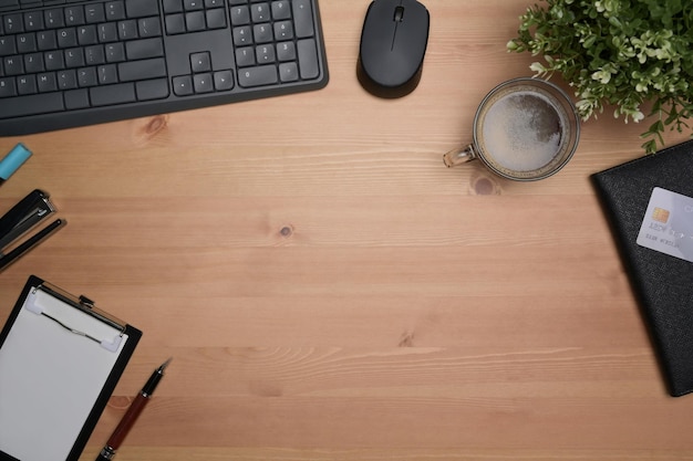 Espacio de trabajo simple de vista superior con bloc de notas, taza de café, tarjeta de crédito y planta de interior en el escritorio de madera