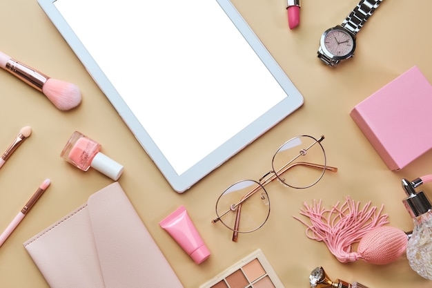 Espacio de trabajo con tableta blanca, bloc de notas, gafas, bolígrafos, accesorios de belleza en superficie beige pastel