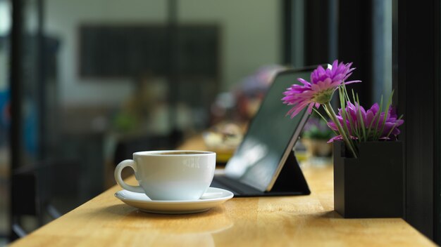 Espacio de trabajo con taza de café, decoración y tableta digital en barra de mostrador en cafetería