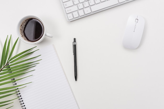 Espacio de trabajo con teclado de computadora, material de oficina, hoja verde y taza de café