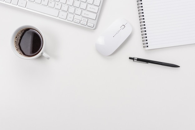 Espacio de trabajo con teclado de computadora, suministros de oficina y taza de café