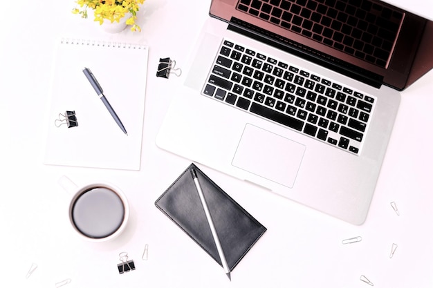 Espacio de trabajo con teclado portátil, diario, café, vasos y flores en el fondo blanco. Plano, vista superior