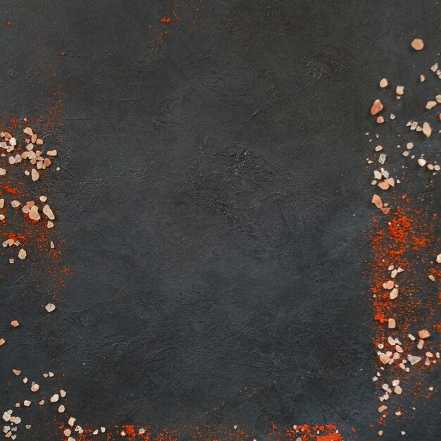 Espacio vacío enmarcado con trozos de fondo oscuro de sal y pimiento rojo o condimentos de especias de pimentón superficie de textura áspera concepto de preparación y cocina de alimentos