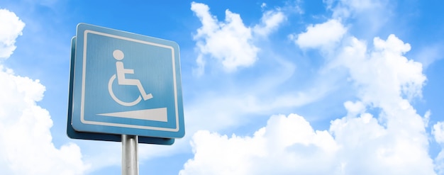 Espaço de estacionamento para deficientes físicos e sinal de cadeira de rodas e símbolos em um mastro alertando os motoristas no fundo do céu azul.
