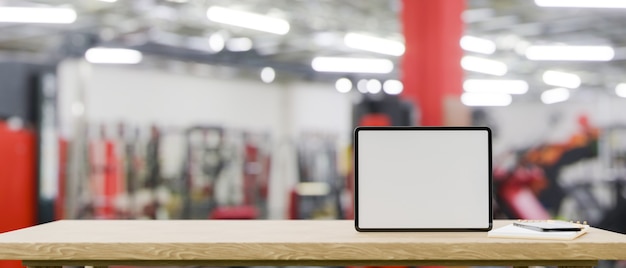 Espaço de maquete na mesa de madeira com maquete de tablet de tela em branco sobre o ginásio de fitness borrado