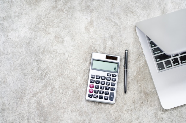 Espaço de trabalho com calculadora, caneta, laptop em concreto cinza