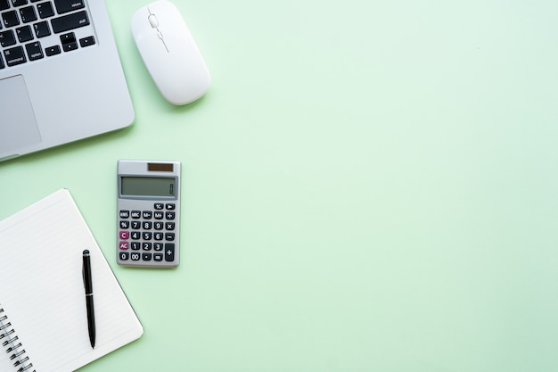 Foto espaço de trabalho com calculadora, caneta, laptop, nota sobre o fundo verde pastel.