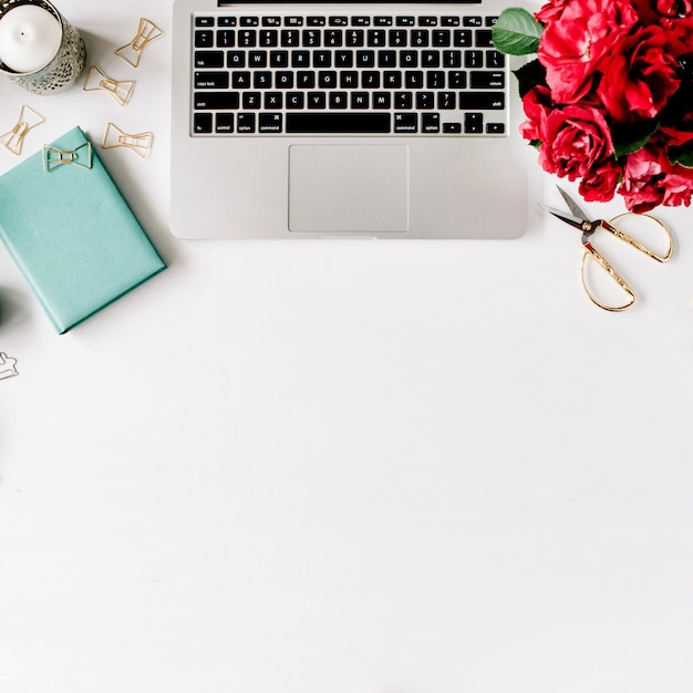 Foto espaço de trabalho com laptop, buquê de rosas vermelhas, diário de hortelã, caneca de café e tesoura dourada em branco