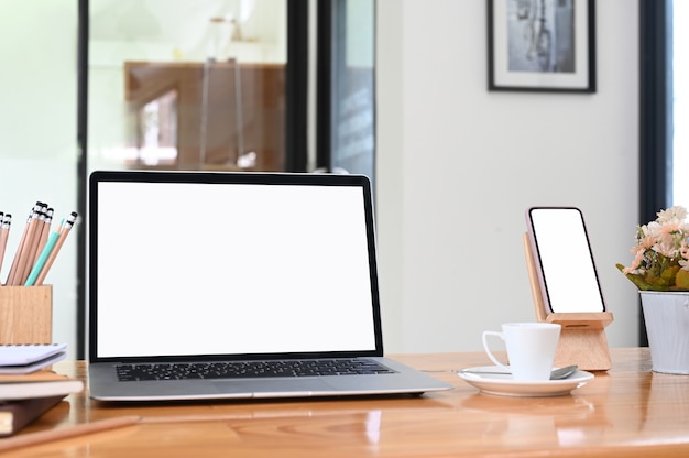 Espaço de trabalho com laptop de tela em branco, smartphone, lápis, xícara de café e maconha na mesa de madeira.