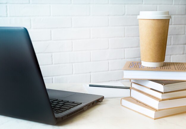 Espaço de trabalho com laptop moderno, livros, café e espaço de cópia.