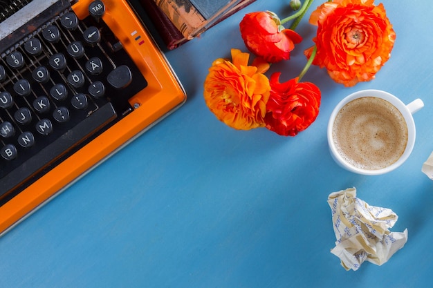 Espaço de trabalho com máquina de escrever vintage laranja com flores e café, copie o espaço no fundo da mesa azul