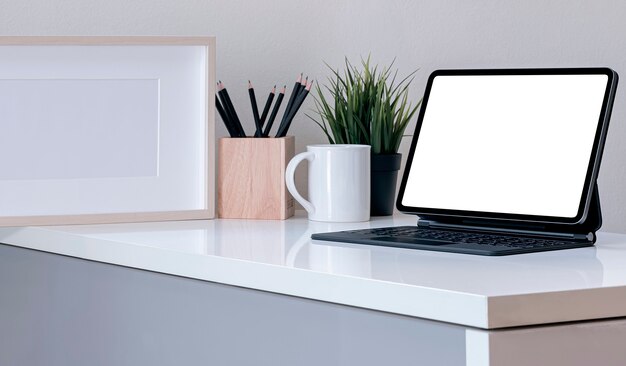 Espaço de trabalho criativo de maquete com tablet de tela em branco e teclado mágico na mesa branca na sala moderna.