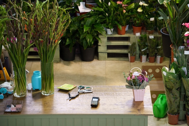 Espaço de trabalho da mesa da floricultura com tesouras para criar buquês dentro da floricultura com plantas em vasos