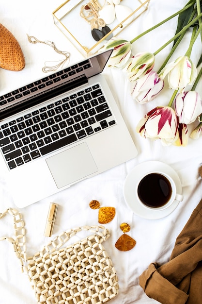 Espaço de trabalho da mesa do escritório doméstico do blog da beleza da moda feminina. Laptop, buquê de flores de tulipa, roupas e acessórios