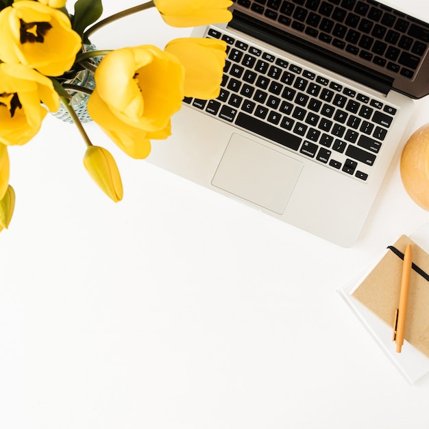 Espaço de trabalho de escritório em casa com laptop, buquê de flores de tulipa amarela, papel de carta em branco