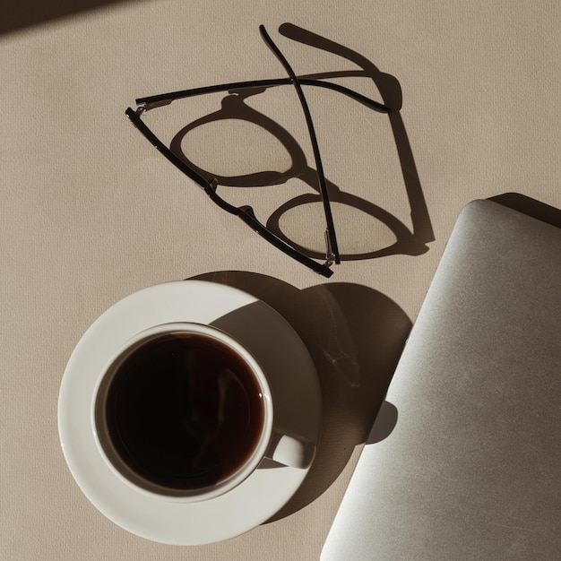 Espaço de trabalho de escritório em casa com óculos de xícara de café de computador portátil em sombras de luz solar Flatlay vista superior estética luxo boêmio mínimo senhora chefe conceito de estilo de vida de negócios