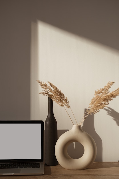 Espaço de trabalho de mesa de escritório em casa estético com sombras de luz solar na parede. Laptop com tela em branco