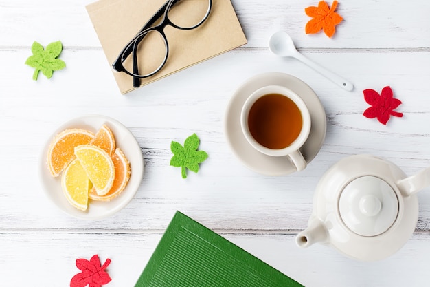 Foto espaço de trabalho de mesa feminina plana leigos com diário, óculos, livro, caneca de chá, doces e decoração de feltro.