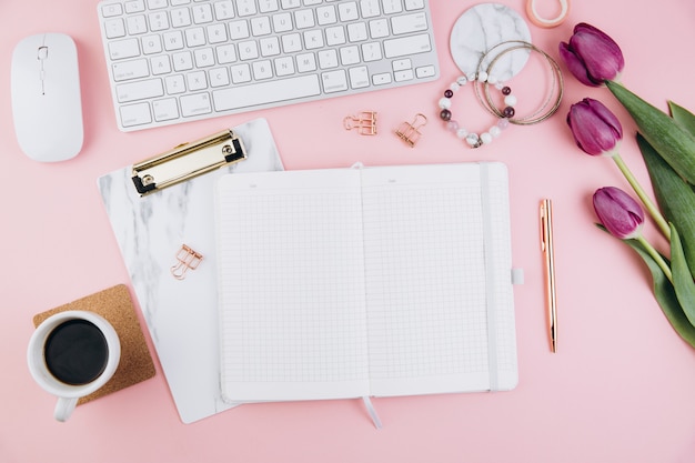 Espaço de trabalho de mesa feminino com tulipas, teclado, clipes de ouro em rosa