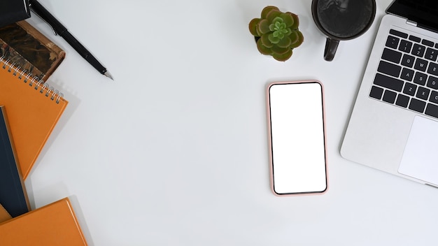 Espaço de trabalho de vista superior com tela vazia de telefone celular e material de escritório na mesa de escritório branca.