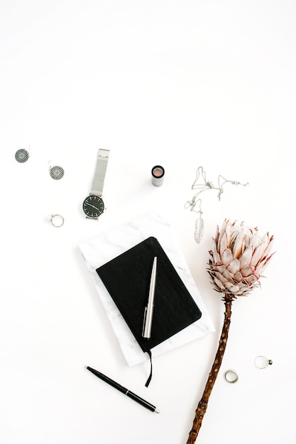 Espaço de trabalho do blogger ou freelancer com flor protea, caderno e acessórios femininos em fundo branco. mesa plana, vista de cima com decoração minimalista e decoração minimalista. conceito de blog de beleza.