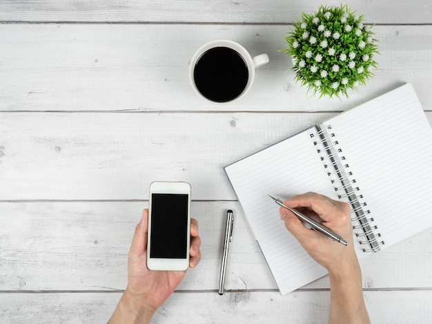 Espaço de trabalho em mesa de madeira branca cópia espaço de cópia; Segure a caneta prata e o smartphone na mão