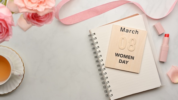Espaço de trabalho feminino com caderno, xícara de chá, flores, fita, batom e mensagem 