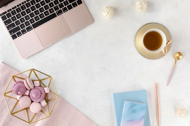 Espaço de trabalho feminino com, laptop, xícara de chá de ervas e sobremesa.