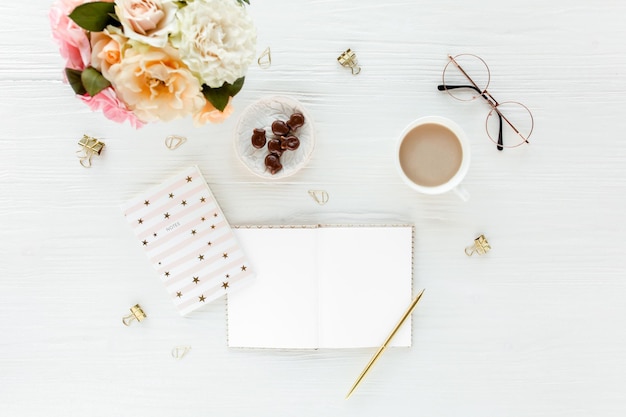 Espaço de trabalho feminino com rosas cor de rosa e bege flores buquê acessórios diário óculos em fundo branco