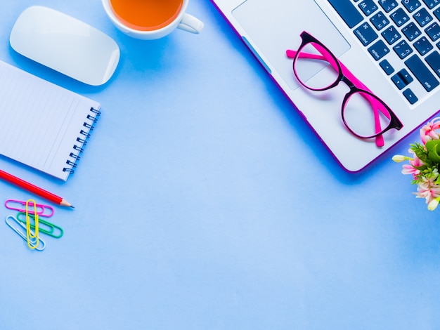 Espaço de trabalho feminino da mesa da vista superior com os acessórios do escritório no fundo azul.