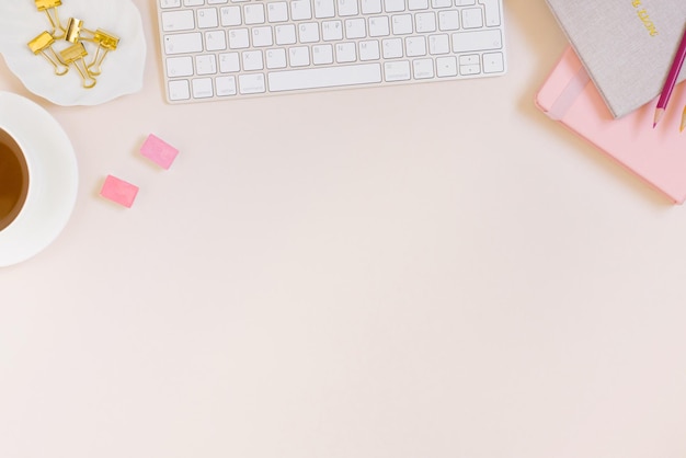 Espaço de trabalho minimalista para mulheres planas com um teclado rosa e bege bloco de notas lápis de cor clipes de papel uma xícara de chá em um fundo bege pastel com um espaço de cópia