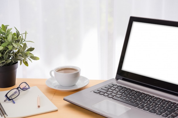 Espaço de trabalho mínimo, computador portátil, xícara de café, vaso verde, óculos e notebook na mesa de madeira