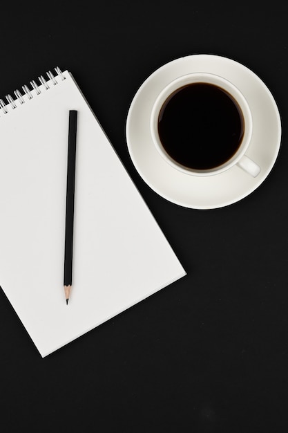 Espaço de trabalho mínimo. Vista superior na mesa de escritório com copo de caderno, lápis e café em um espaço preto.