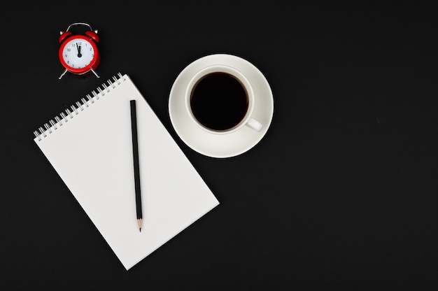 Espaço de trabalho mínimo. Vista superior na mesa de escritório com copo de caderno, lápis e café em um fundo preto.