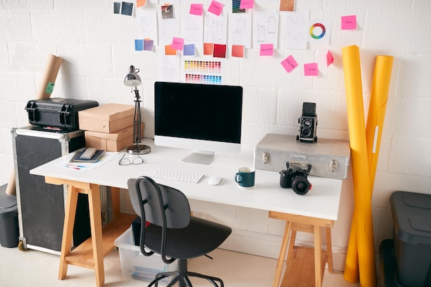 Espaço de trabalho no estúdio criativo com mesa e computador na frente da parede com desenhos de moda