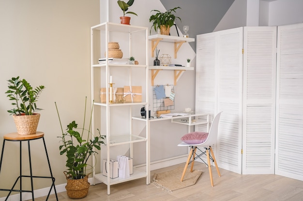 Espaço de trabalho vazio de home office em um apartamento aconchegante com design escandinavo moderno. prateleiras brancas para cadeiras de mesa com elementos de decoração elegantes, artigos de papelaria, plantas de interior em vasos de vime