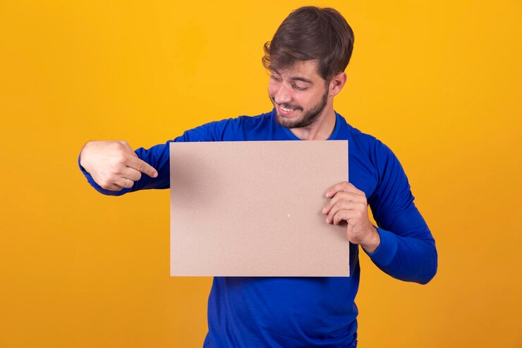 Foto espaço livre para publicidade homem caucasiano feliz apontando para o quadro branco vazio na maquete de fundo amarelo do estúdio